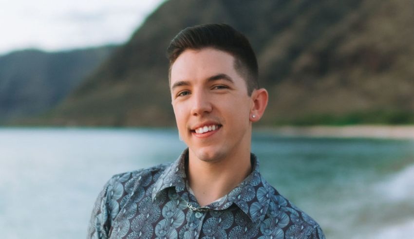 A young man smiling in front of the ocean.