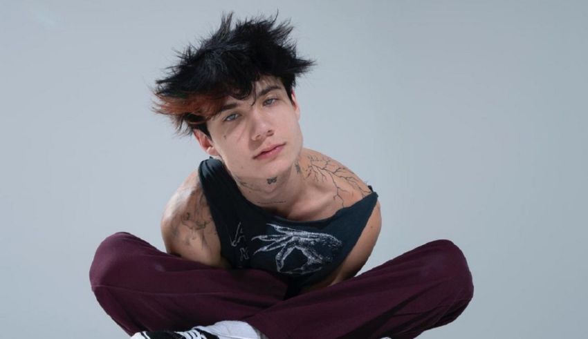 A young man with tattoos sitting on top of a grey background.