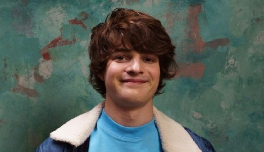 A young man smiling in front of a green wall.