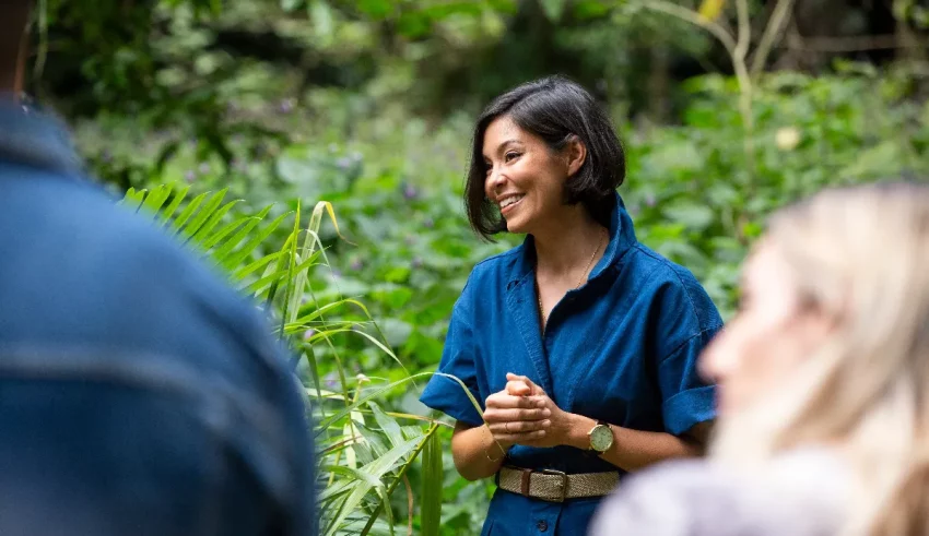 A woman in a blue shirt is talking to a group of people in the jungle.