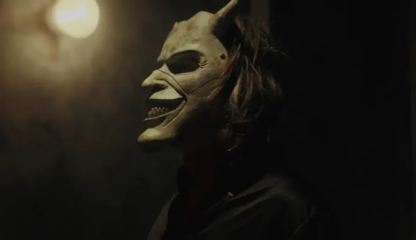 A man in a devil mask standing in a dark room.