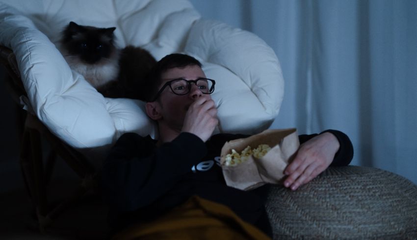 A man sitting in a chair with a cat watching tv.