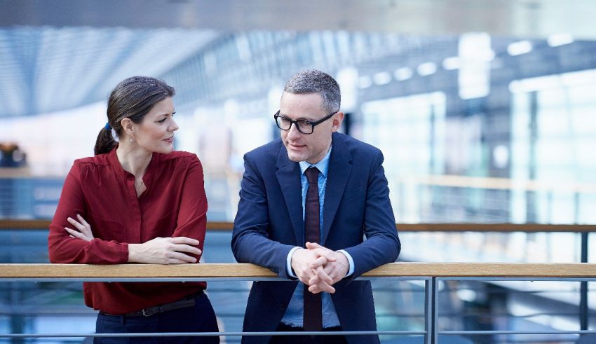 Two business people talking on a railing in an office building.