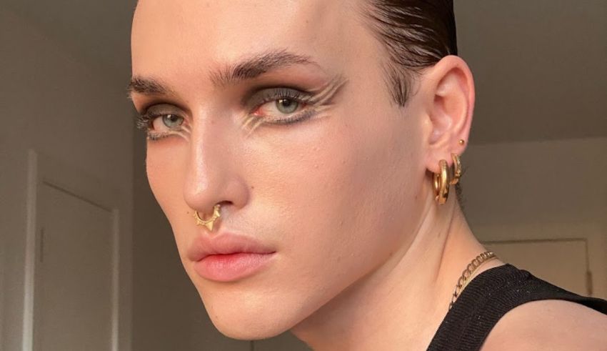 A man with gold ear piercings is posing in front of a mirror.