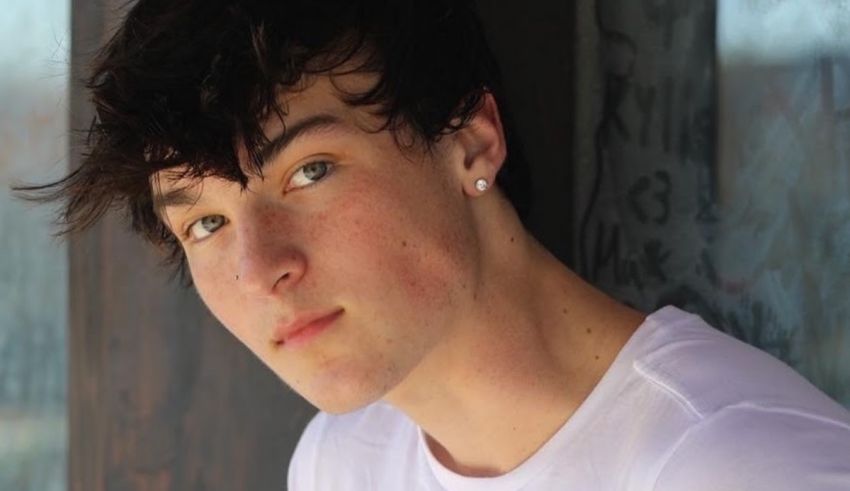 A young man in a white shirt leaning against a wall.