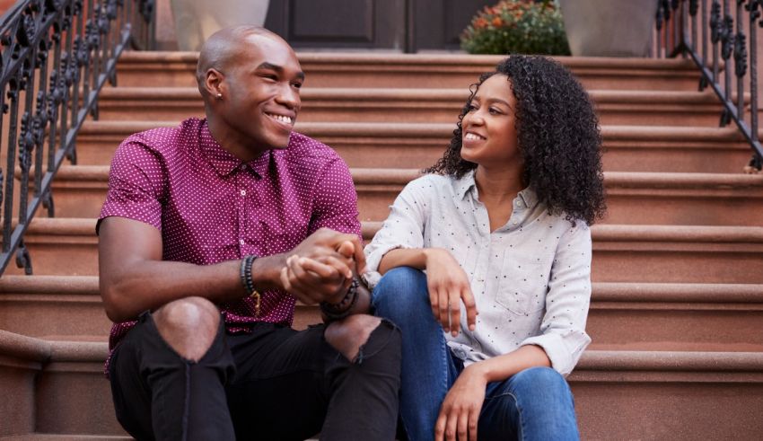 A young black man and woman sitting on the steps of their home.