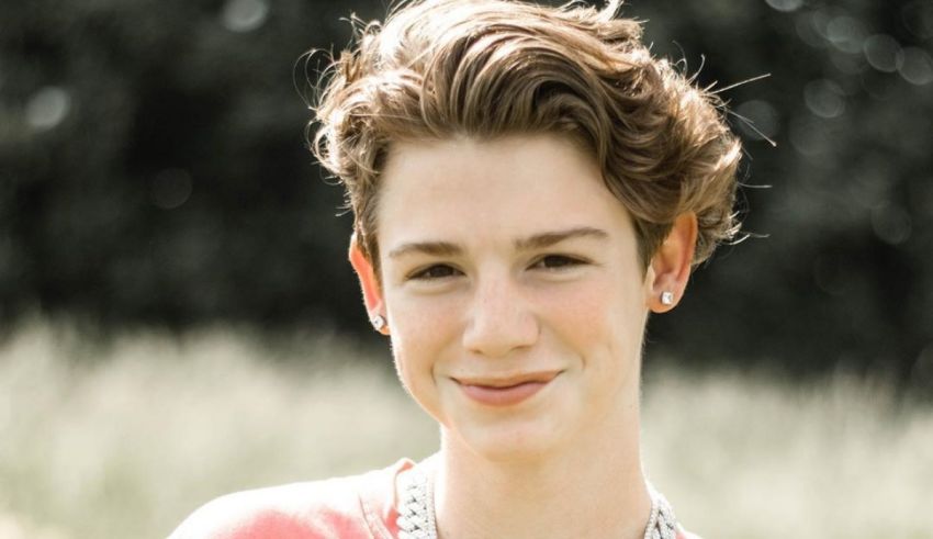 A young man in a pink shirt smiling in a field.