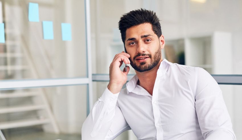 A man is talking on the phone while sitting at a desk.