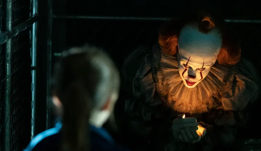 A clown is looking at a girl in a cage.