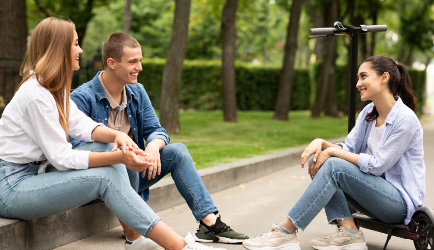 A group of young people sitting on a sidewalk talking to each other.