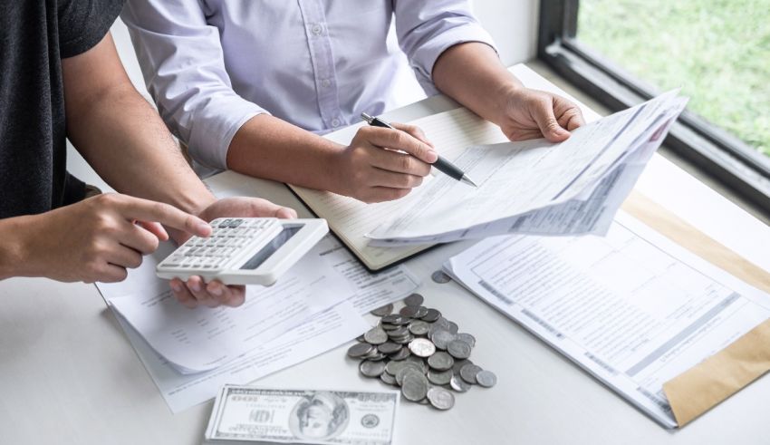 Two people sitting at a desk with money and a calculator.