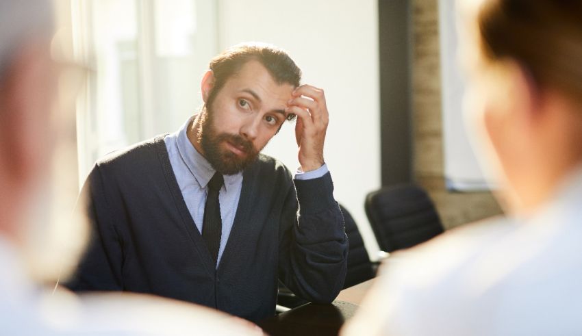 A man in a business meeting is looking at his head.