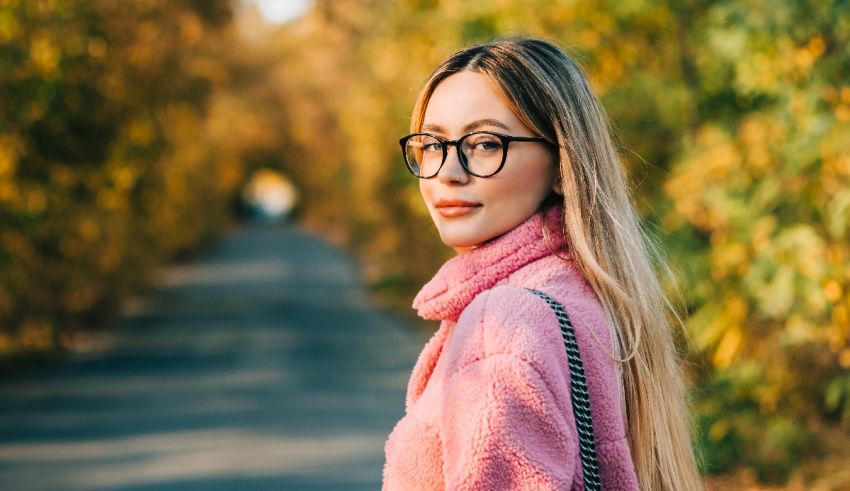 A beautiful young woman wearing glasses and a pink sweater.