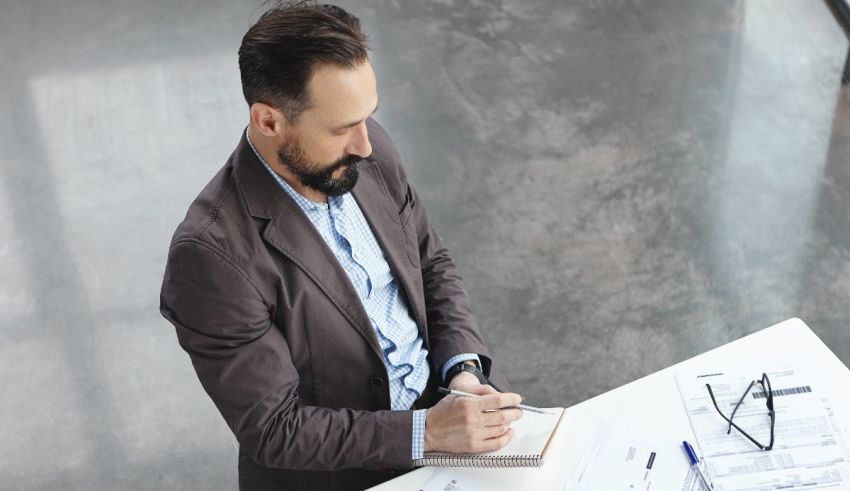 A man is writing in a notebook at a desk.