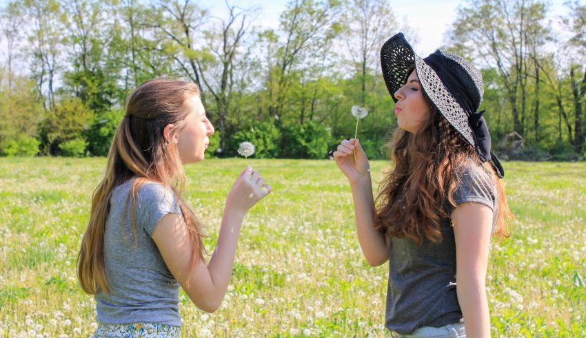 Two girls blowing dandelion seeds in a field.