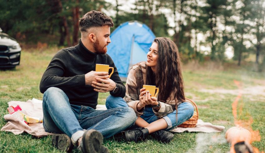 A couple sitting around a campfire with a cup of coffee.