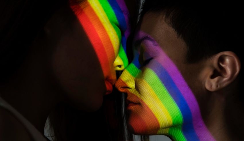 A man and woman kissing in front of a rainbow colored background.