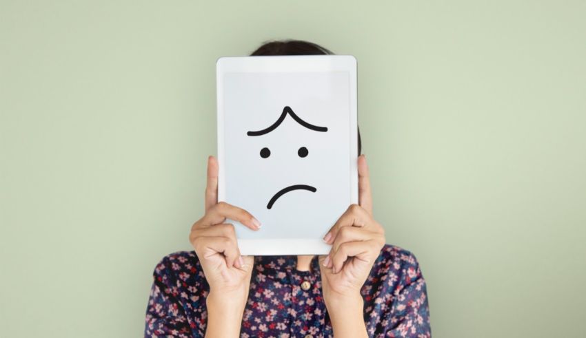 A woman holding a tablet with a sad face on it.