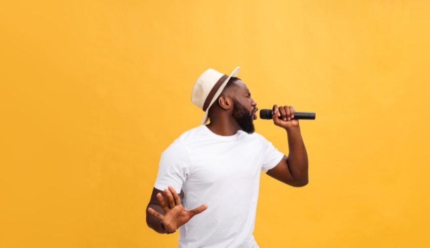 A black man singing into a microphone against a yellow background.