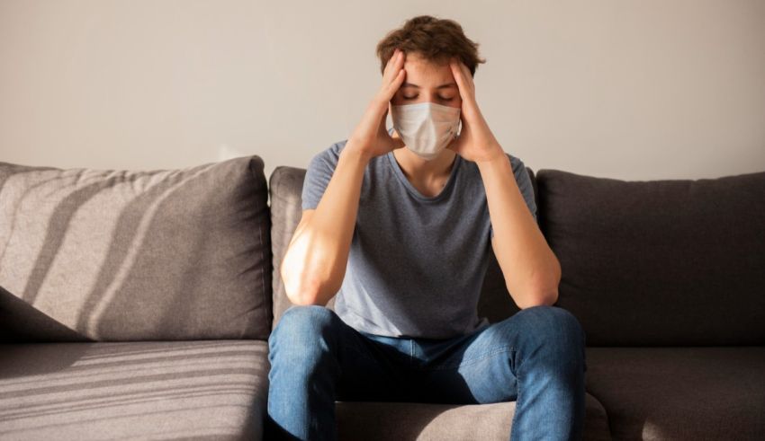 A young man sitting on a couch with a face mask on.