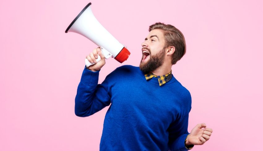 A man shouting into a megaphone on a pink background.