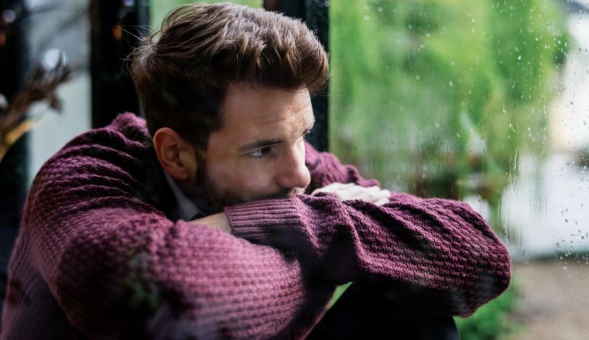 A man looking out a window in a rainy day.