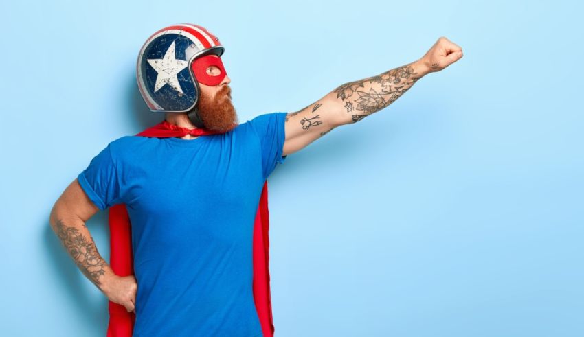A bearded man in a superhero costume pointing at the camera.