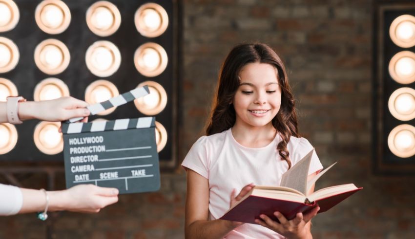 A girl is reading a book while holding a clapper board.