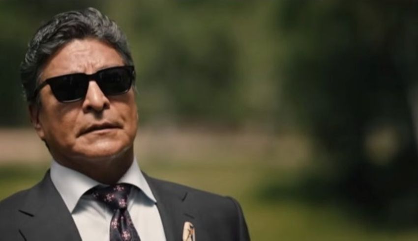 A man in a suit and sunglasses is standing in a field.