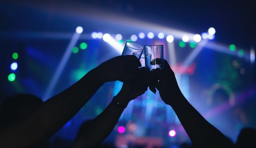 Two people toasting glasses in front of a stage at a concert.