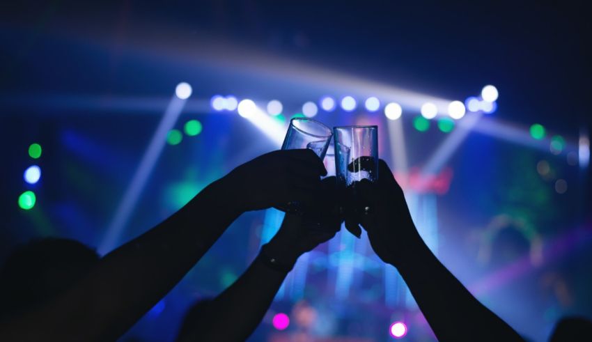 Two people toasting glasses in front of a bright light at a concert.