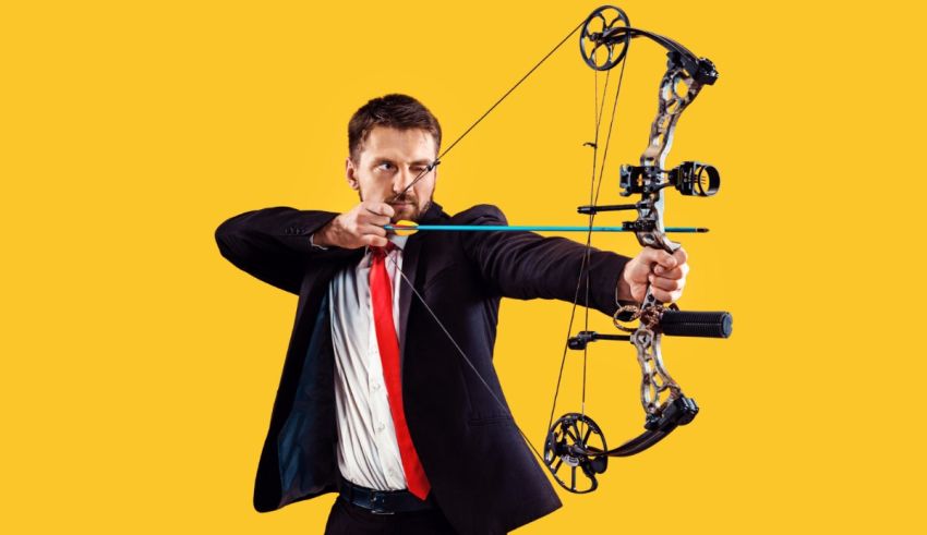 A man in a suit is aiming at a bow and arrow.