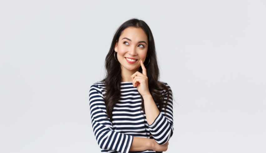 A young woman in a striped shirt is posing with her hand on her chin.