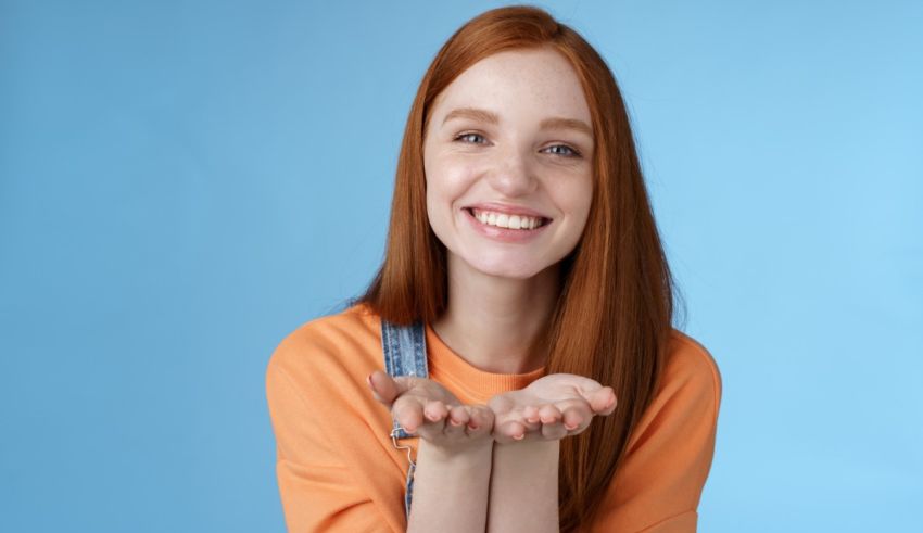 A young girl with red hair is holding her hands in front of her face.