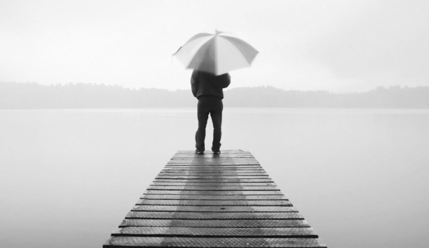 A person standing on a dock with an umbrella.