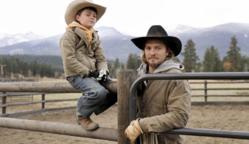 Two men in cowboy hats sitting on a fence.