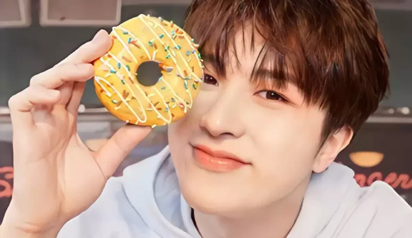 A young man holding up a donut with sprinkles on it.