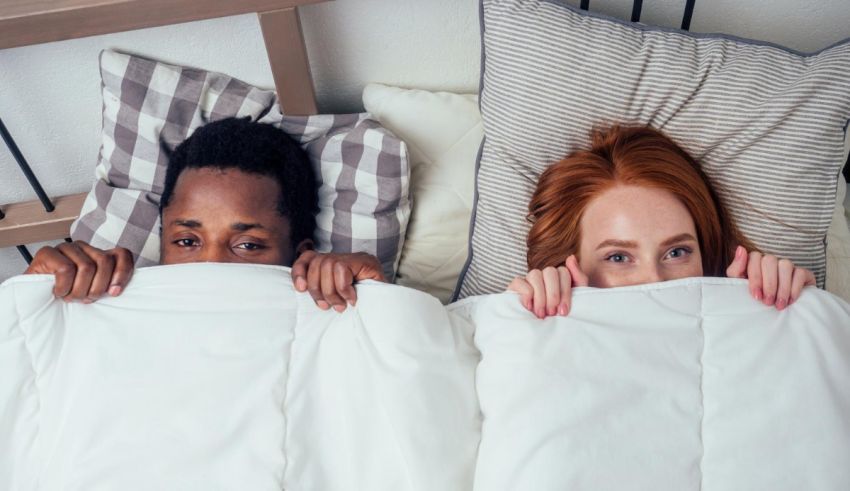 A man and woman are hiding under a blanket in bed.