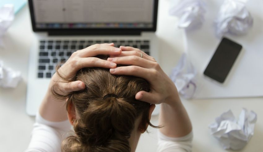 A woman is holding her head in front of a laptop.