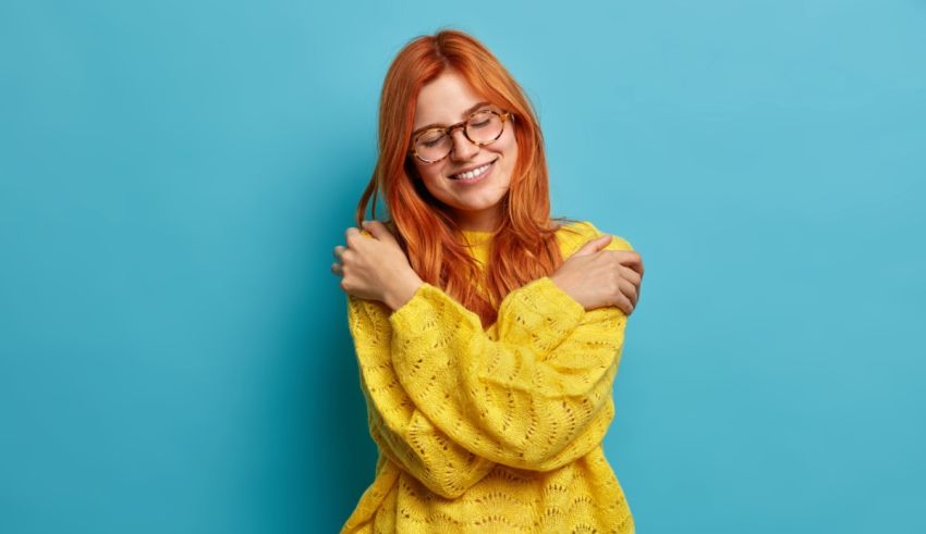 A young woman with red hair and glasses is posing against a blue background.