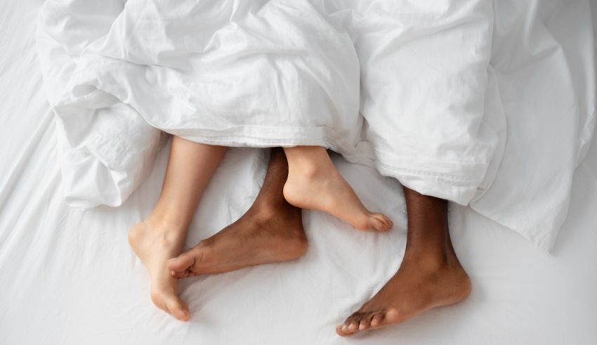 Two people's feet are laying on a bed with white sheets.