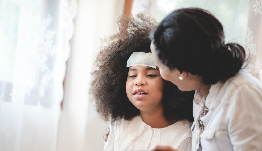A young girl with afro hair is being helped by her mother.