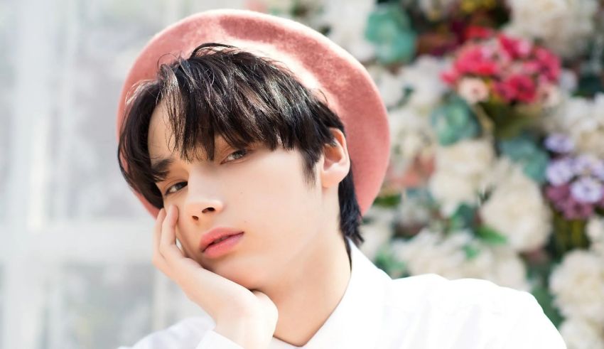 A young man in a pink hat leaning against a flower.