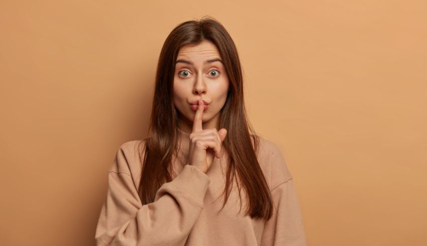 A young woman making a hush sign on a beige background.