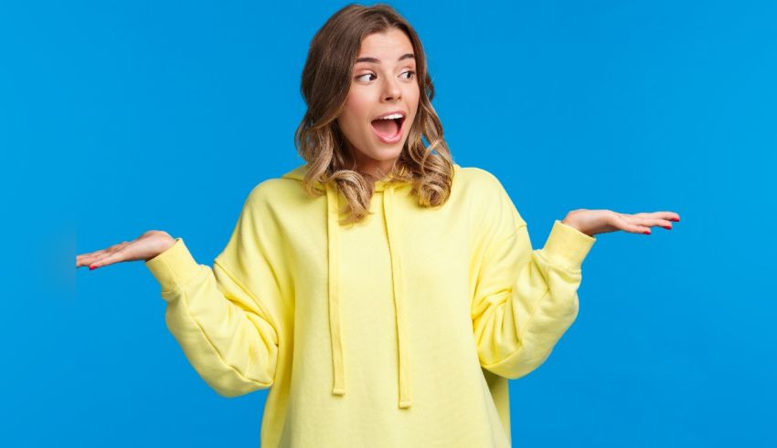 A young woman in a yellow sweatshirt with her hands outstretched on a blue background.