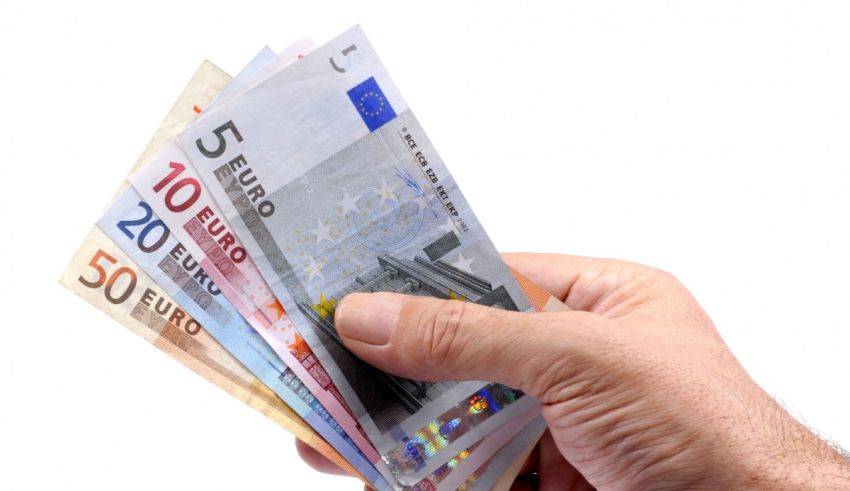 A man's hand holding a bunch of euro banknotes.