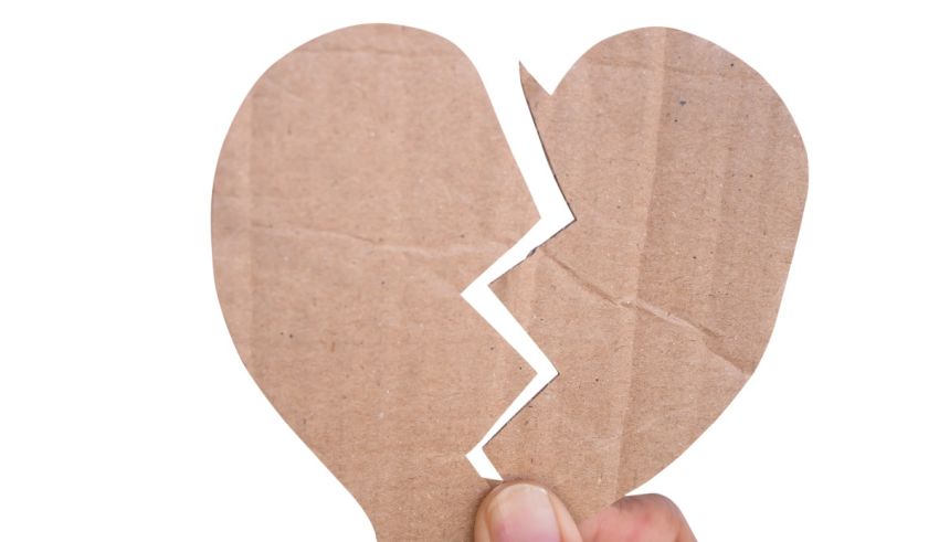 A person holding a broken cardboard heart on a white background.