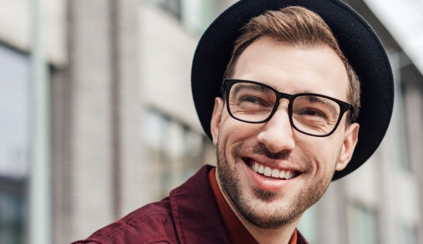 A man wearing glasses and a hat is smiling.