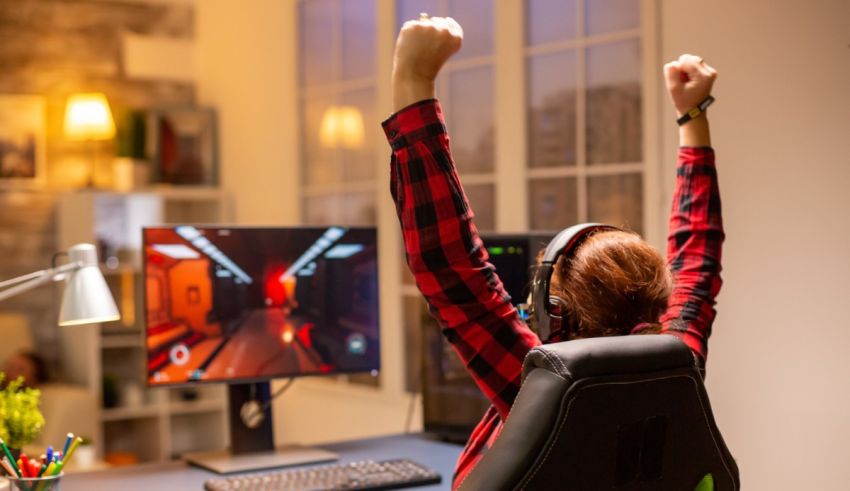 A woman in a red shirt is raising her arms in front of a computer screen.