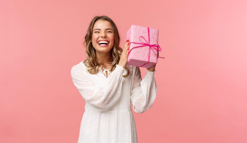 A young woman holding a pink gift box on a pink background.